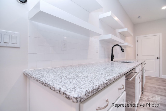kitchen featuring open shelves, a sink, light wood-style floors, white cabinetry, and backsplash