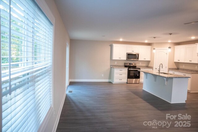 kitchen with a sink, stainless steel appliances, dark wood finished floors, baseboards, and white cabinetry