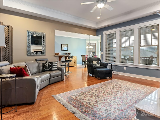 living area with a ceiling fan, wood finished floors, a tray ceiling, baseboards, and ornamental molding