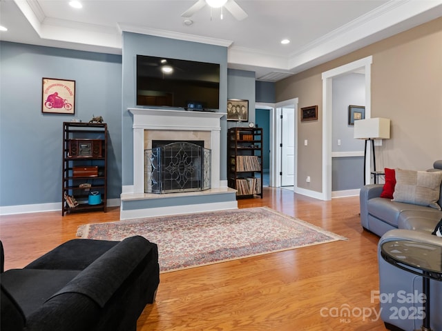 living area with a tray ceiling, wood finished floors, crown molding, and a ceiling fan