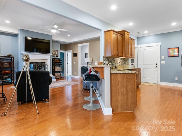 kitchen featuring light stone counters, light wood-style floors, ceiling fan, and crown molding