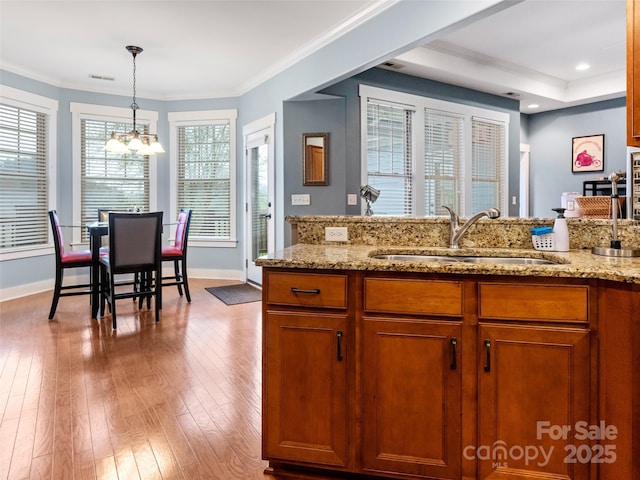 kitchen with a sink, light stone countertops, pendant lighting, a chandelier, and brown cabinetry