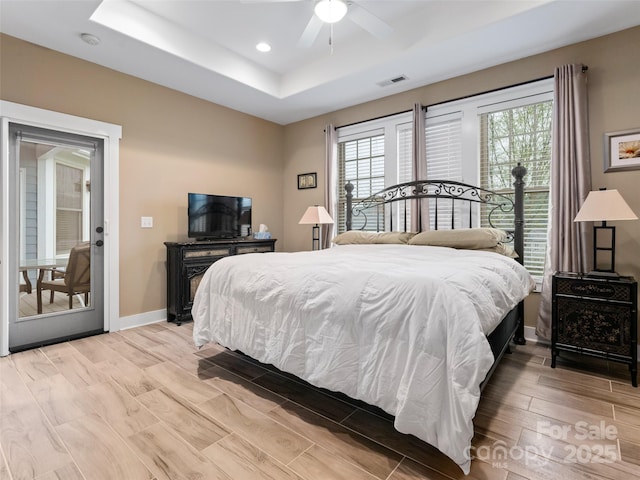 bedroom featuring light wood-type flooring, a tray ceiling, baseboards, visible vents, and recessed lighting