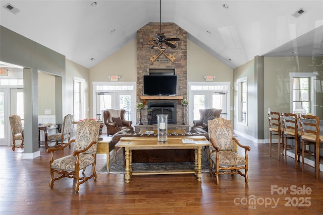 living room featuring wood finished floors, visible vents, a ceiling fan, and a stone fireplace
