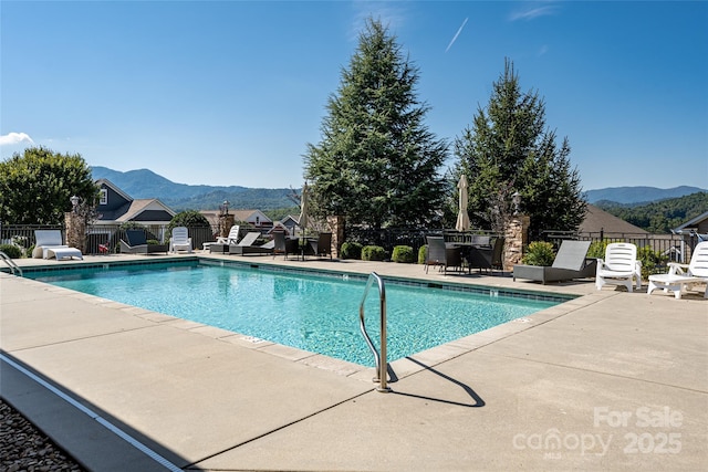 community pool with a patio, fence, and a mountain view