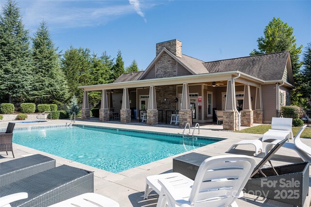 community pool with a patio area, an outdoor bar, a ceiling fan, and fence