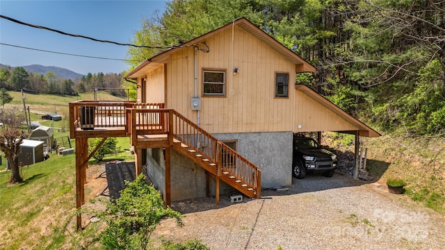 back of property with stairway, gravel driveway, a deck with mountain view, and a carport