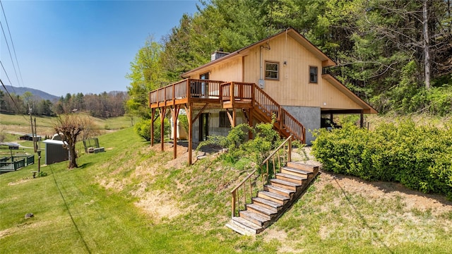 rear view of house with a lawn, a wooden deck, stairs, and a forest view