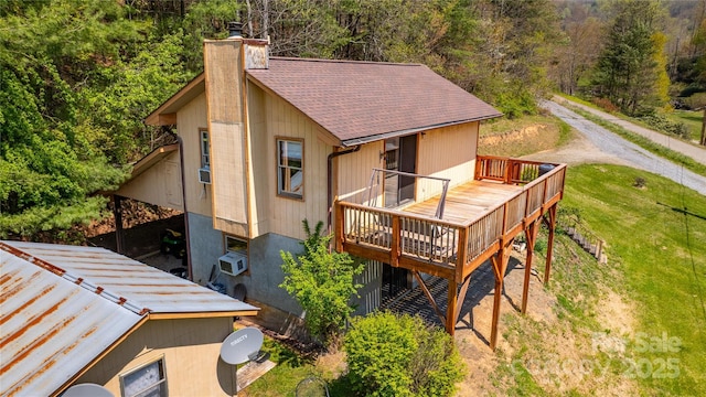 back of property with a forest view, a chimney, a yard, a wooden deck, and roof with shingles