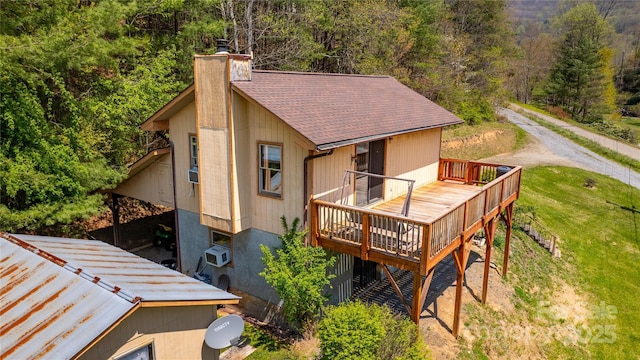 back of property with a chimney, a yard, roof with shingles, a forest view, and a deck