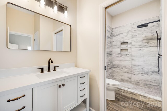 full bathroom with wood finished floors, toilet, vanity, and tiled shower