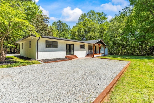 view of front of house with covered porch, driveway, french doors, brick siding, and a front lawn