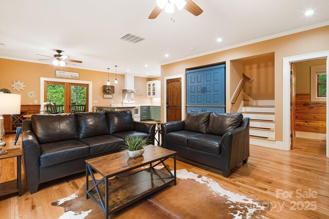 living area with a ceiling fan, stairs, light wood-style flooring, and visible vents