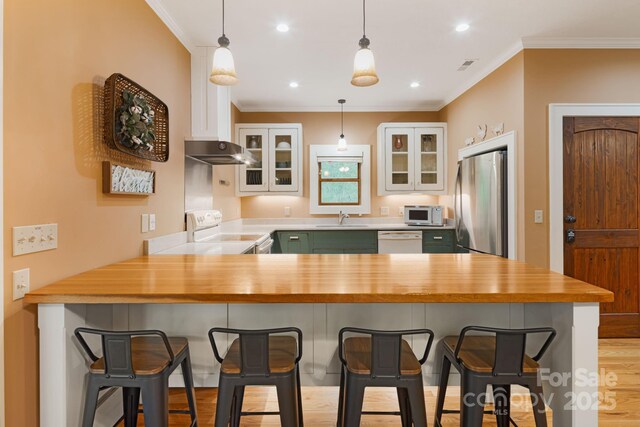 kitchen featuring crown molding, a peninsula, white appliances, white cabinetry, and a sink
