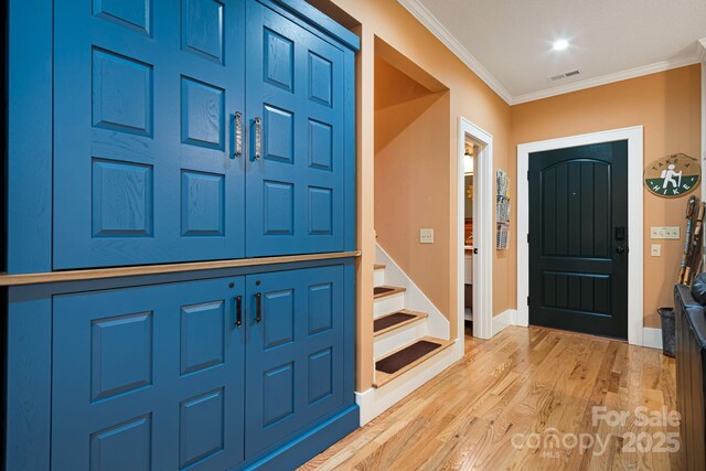 entryway featuring visible vents, ornamental molding, stairs, wood finished floors, and baseboards
