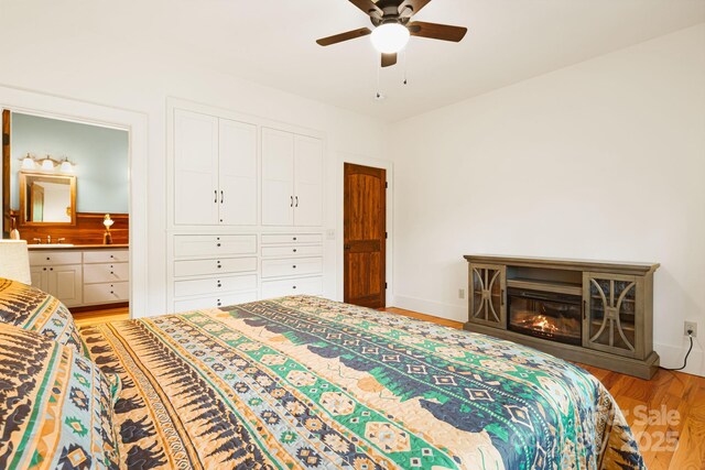 bedroom with ceiling fan, a sink, light wood-style floors, baseboards, and ensuite bathroom