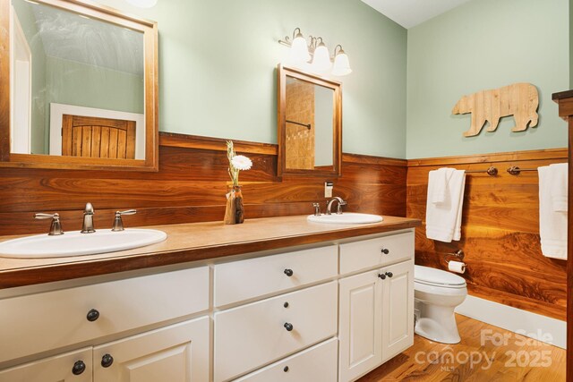 bathroom featuring a sink, toilet, double vanity, and wood finished floors