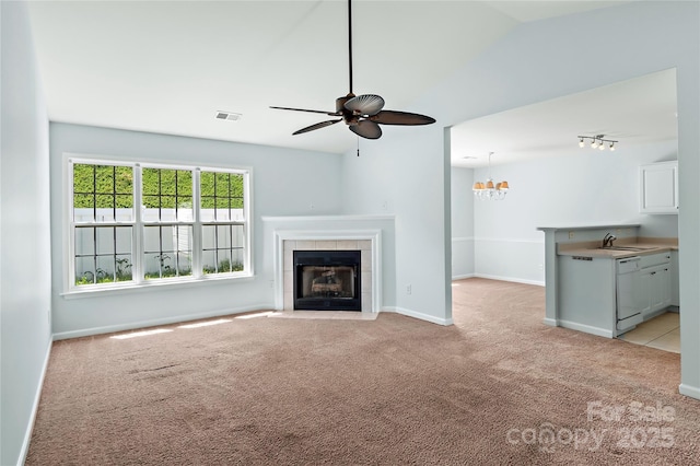 unfurnished living room featuring a ceiling fan, a sink, a tiled fireplace, light colored carpet, and visible vents