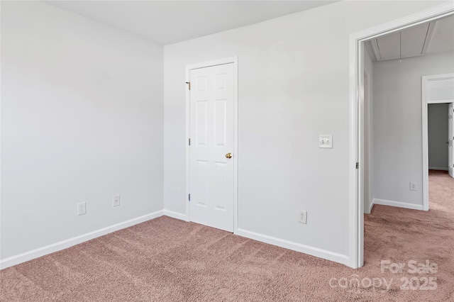 carpeted empty room with attic access and baseboards