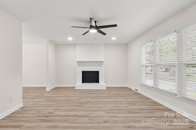 unfurnished living room with ceiling fan, a fireplace, plenty of natural light, baseboards, and light wood-type flooring