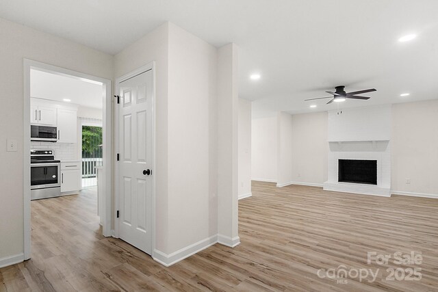 unfurnished living room with light wood-style floors, a ceiling fan, baseboards, and a brick fireplace