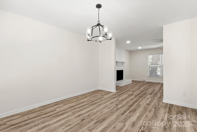 unfurnished living room with a fireplace, light wood-style floors, baseboards, recessed lighting, and a notable chandelier