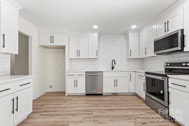 kitchen featuring light wood-type flooring, white cabinetry, a sink, backsplash, and stainless steel appliances