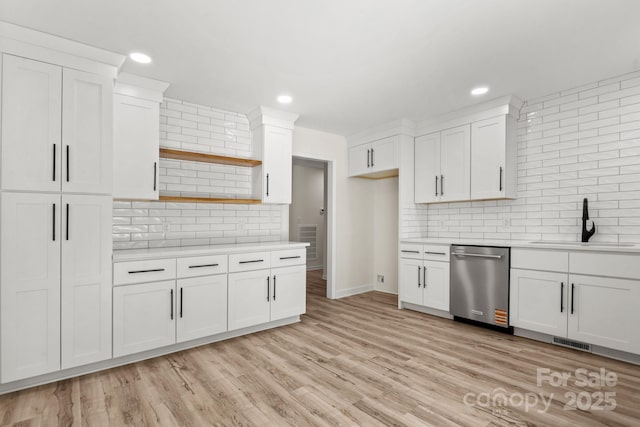 kitchen featuring stainless steel dishwasher, backsplash, a sink, and light countertops