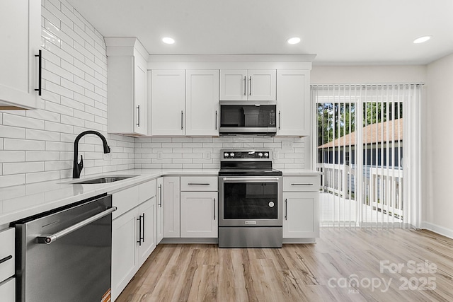 kitchen with light countertops, white cabinetry, a sink, light wood finished floors, and stainless steel appliances