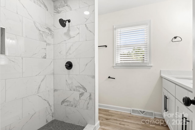full bath featuring a tile shower, vanity, baseboards, wood finished floors, and visible vents