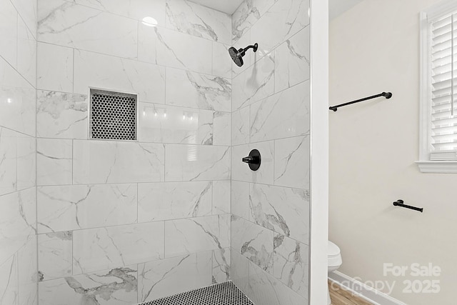 bathroom featuring toilet, baseboards, tiled shower, and wood finished floors