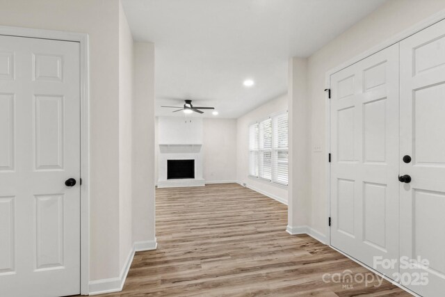 interior space featuring ceiling fan, baseboards, a fireplace with raised hearth, recessed lighting, and light wood-style flooring