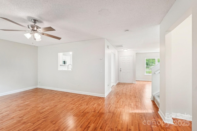unfurnished room with light wood-style flooring, a textured ceiling, and baseboards