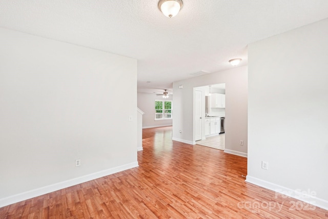spare room featuring light wood-type flooring, a ceiling fan, and baseboards