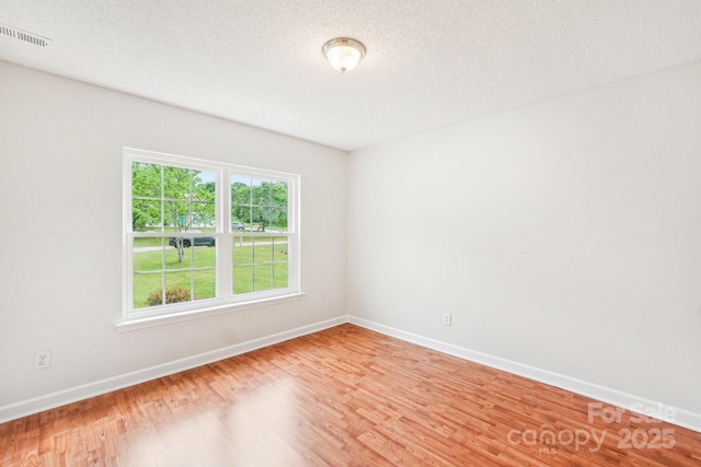 empty room with a textured ceiling, light wood-type flooring, visible vents, and baseboards