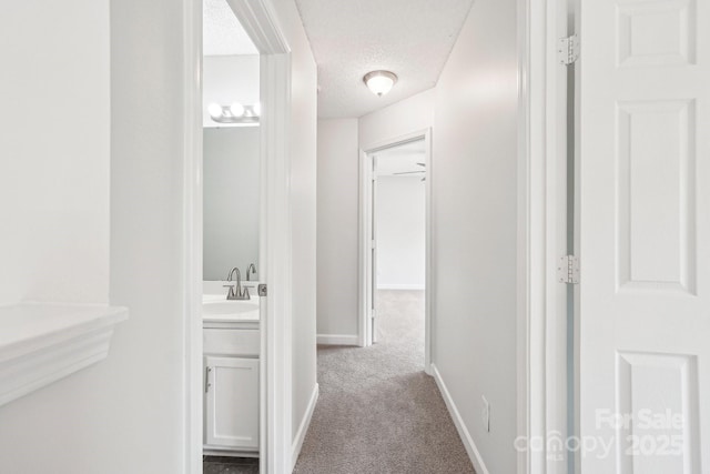 hallway featuring carpet, baseboards, a sink, and a textured ceiling