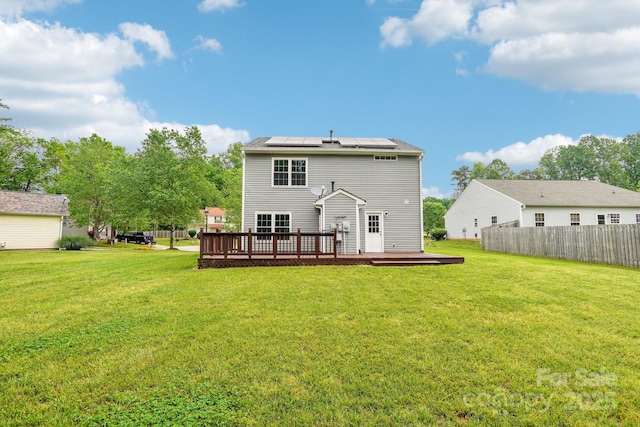 rear view of house with a lawn, a wooden deck, solar panels, and fence