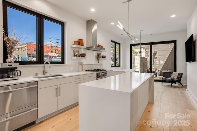kitchen with wall chimney range hood, open shelves, a sink, light wood-type flooring, and appliances with stainless steel finishes