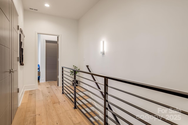 hall with an upstairs landing, light wood-style floors, baseboards, visible vents, and recessed lighting