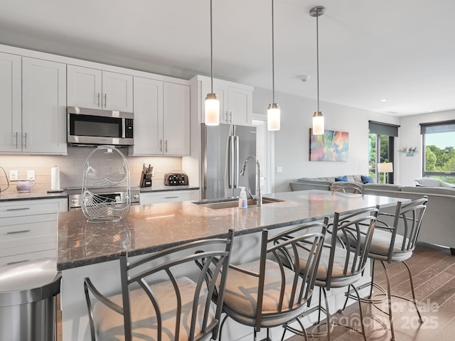 kitchen with a kitchen bar, tasteful backsplash, dark stone countertops, open floor plan, and stainless steel appliances