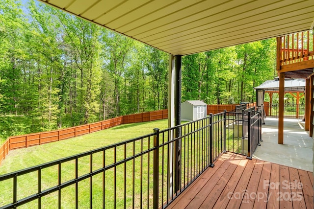 deck featuring a fenced backyard, an outdoor structure, a lawn, a storage unit, and a gazebo