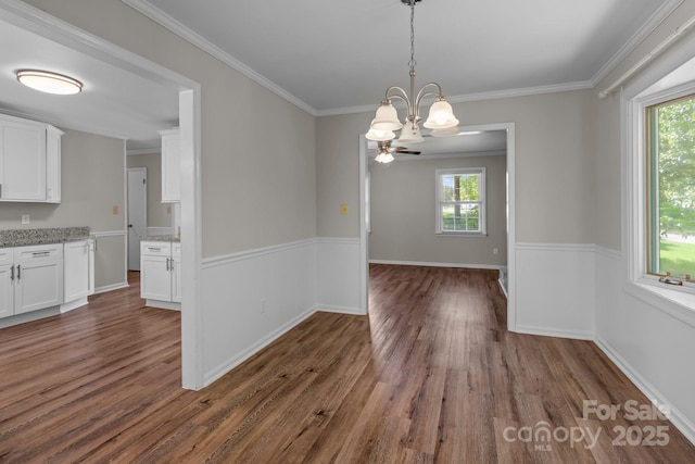 unfurnished dining area featuring crown molding, a healthy amount of sunlight, wood finished floors, and a chandelier