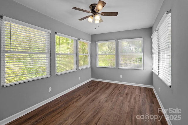 empty room featuring dark wood-type flooring, a healthy amount of sunlight, baseboards, and ceiling fan