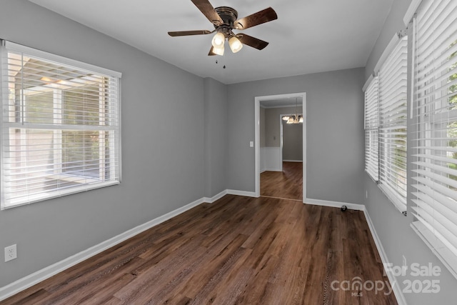 unfurnished bedroom featuring baseboards, wood finished floors, multiple windows, and ceiling fan with notable chandelier