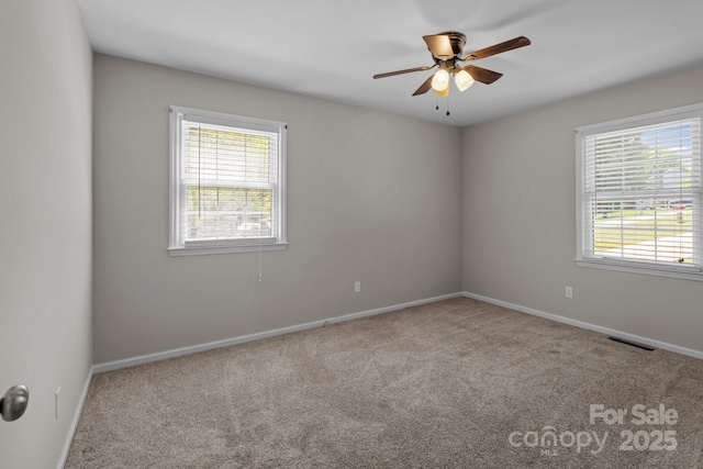 carpeted spare room featuring baseboards, visible vents, a wealth of natural light, and ceiling fan