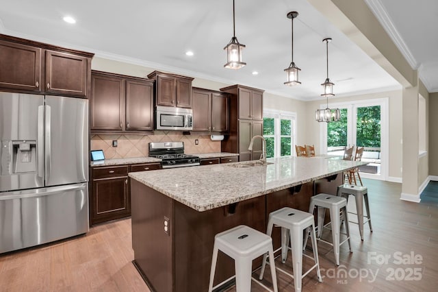 2417 Labelle Dr, Waxhaw, NC 28173 - kitchen featuring stainless steel appliances, light wood-style floors, backsplash, a kitchen island with sink, and crown molding