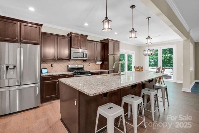 2417 Labelle Dr, Waxhaw, NC 28173 - kitchen with stainless steel appliances, light wood-style flooring, decorative backsplash, a kitchen island with sink, and crown molding