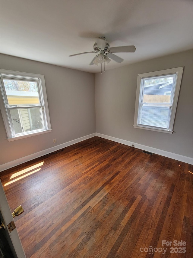 unfurnished room featuring baseboards, a ceiling fan, dark wood-type flooring, and visible vents