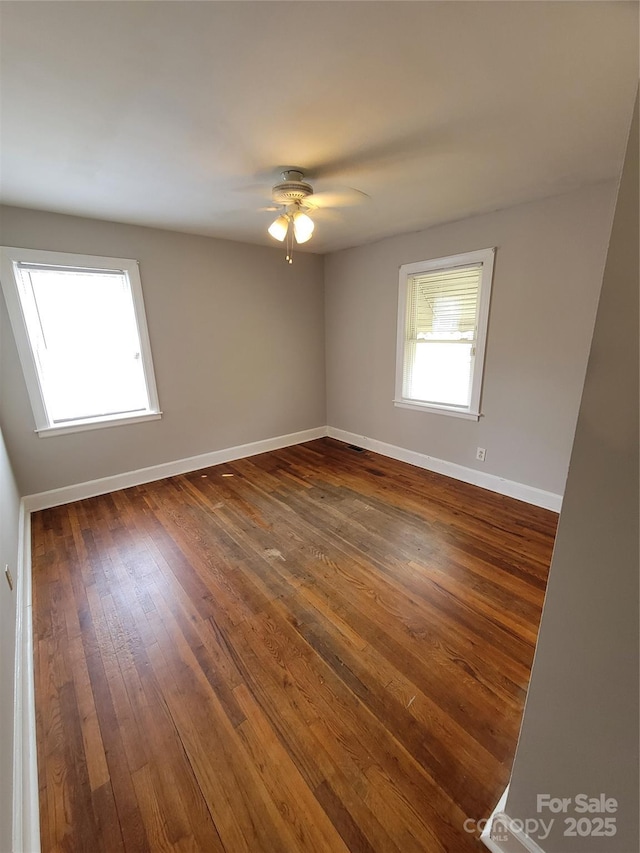 empty room with baseboards, a ceiling fan, and dark wood-style flooring