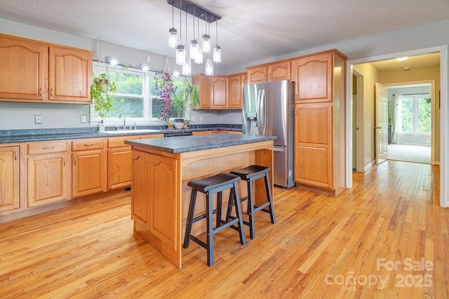 kitchen featuring dark countertops, stainless steel fridge with ice dispenser, light wood-type flooring, and a sink